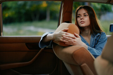 Thoughtful young woman in a denim jacket looking out of a vintage car window, showcasing emotions...