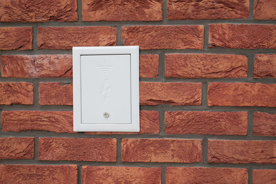 Electrical box on a brick wall Cover is white and mounted flush Weatherproofed for outdoor use Grounding symbol visible