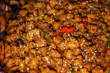 An appetizing close-up showcases seasoned and glazed chicken pieces, sprinkled with sesame seeds. The dish features subtle hints of green and red peppers, creating visual interest and depth.