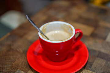 A close-up shot captures a vibrant red cup and saucer against a wooden surface, showcasing a creamy...