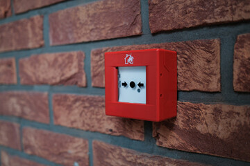 Close up of a red emergency fire alarm switch mounted on a brick wall featuring a white activation...