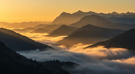 Obraz premium Evening mountain landscape with fog rolling through valleys, low sun casting golden hue