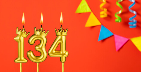 Number 134 birthday candle on an orange background with pennants