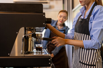 Asian woman entrepreneur making coffee from machine while standing by coworker at cafe. Female barista making coffee in coffee shop counter. Takeaway food. Professional coffee making. Small business.