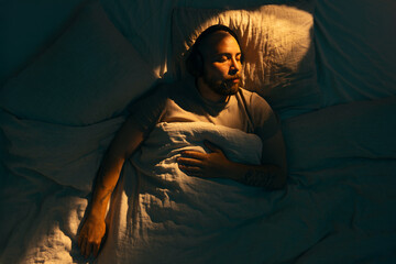A caucasian man with a beard peacefully sleeping in bed, wearing wireless headphones