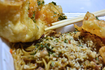 Close-up of seasoned noodles topped with crushed peanuts and served with crispy fried wontons in a...