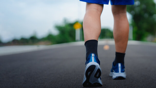 Close-up of a young man walking on an asphalt road wearing blue running shoes and black socks. Concept of fitness, outdoor exercise, healthy lifestyle, and physical activity in a natural setting.