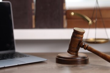 Judge. Laptop, gavel and scales on wooden table in office, selective focus
