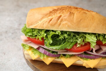 Tasty baguette sandwich with ham, cheese and vegetables on grey table, closeup