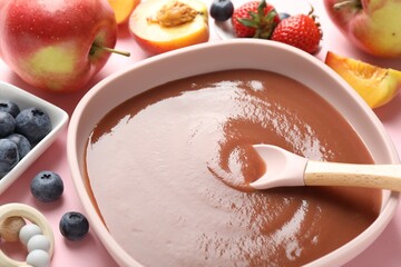 Baby food. Eating tasty puree with spoon at pink table, closeup