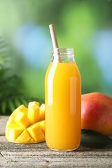 Tasty mango juice in glass bottle and fresh fruits on wooden table against blurred background