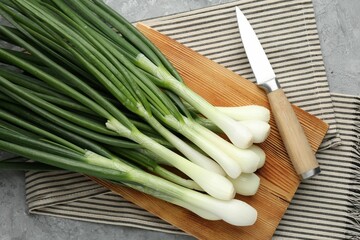 Fresh ripe green onions with cutting board and knife on grey table, flat lay