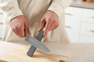 Man sharpening knife with sharpener at beige table indoors, closeup
