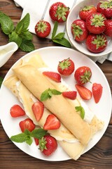 Tasty crepes with cream, strawberries and mint on wooden table, flat lay