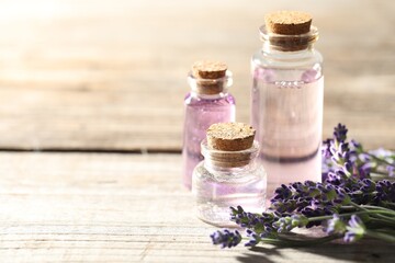 Natural essential oil and lavender flowers on wooden table, closeup. Space for text