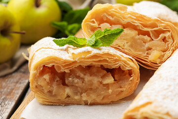 Tasty apple strudels with powdered sugar, mint and fruits on table, closeup