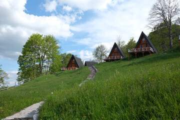 A frame cabins dot a green hillside under a bright sky accessible by a stone path Serene rural...