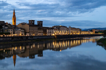 Illuminated buildings along the Arno River reflecting on the water during blue hour in Florence city center, Italy