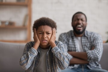 Obraz premium Furious dad yells at terrified son on the couch boy cries and covers ears Child abuse at home Focused shot