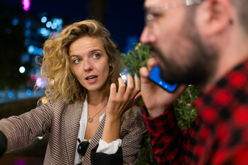 Young woman engaged in animated conversation while man uses smartphone at night in urban setting