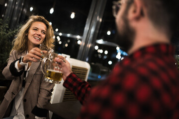 Smiling friends enjoying a night out at a cozy pub, toasting with beer glasses, surrounded by warm...
