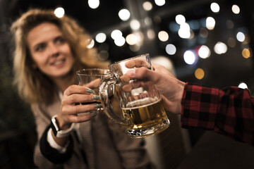 Cheers with friends in a cozy evening setting, celebrating with a clink of beer mugs in a warm, inviting ambiance. Bokeh lights create a festive backdrop for a joyful social gathering.
