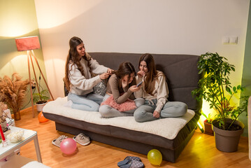 Three young women spending quality time together in a cozy living room setting, engaging and...