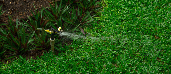 Automatic lawn sprinkler system watering green grass in residential garden with water droplets...