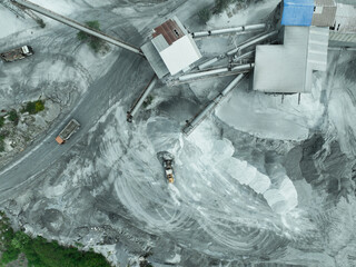 Aerial view of granite and limestone crushing plant with dump trucks and excavators processing raw stone into construction aggregates for concrete and infrastructure development. Stone mill factory.