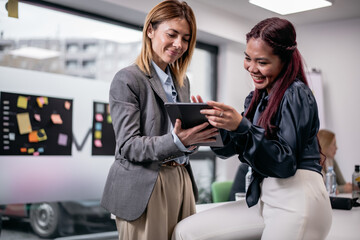 Two professional women collaborating and sharing ideas on a digital tablet in a modern and creative...