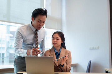 Asian business professionals discuss project analysis strategy on laptop during collaborative office meeting