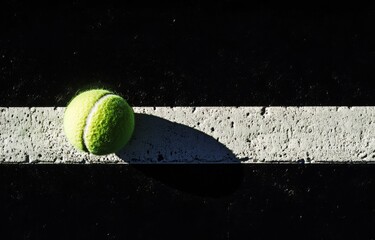 Tennis ball on court line, shadow, sunlight.