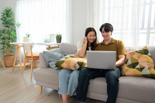 Asian young couple using laptop computer in living room at home.