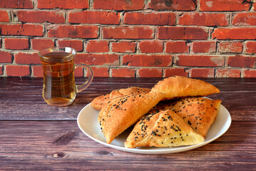 A cup of hot black tea and a plate with a bunch of samosa meat pies on a wooden table.