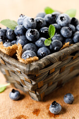Ripe blueberries in wicker basket on wooden table.