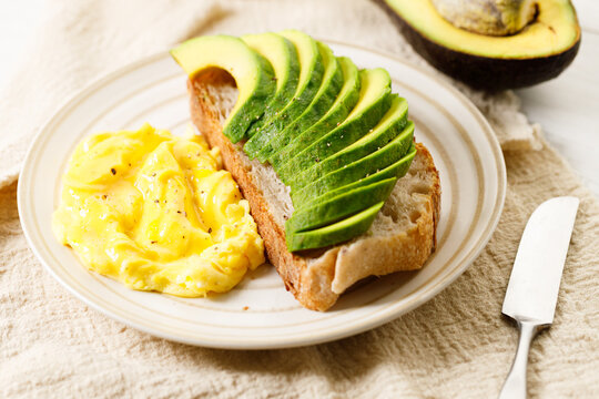 Healthy simple breakfast toast with sliced avocado and scrambled egg.