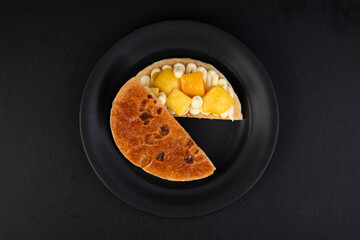 Cake with fruit on a black plate, isolated on black background