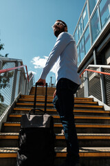Businessman climbing stairs with trolley luggage at train station