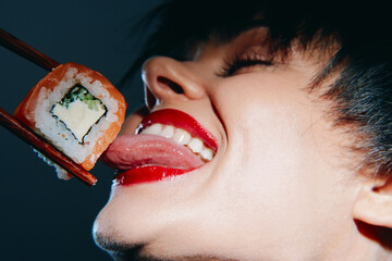 A close-up of a woman enjoying sushi with vibrant red lips, showcasing excitement and indulgence while holding sushi with chopsticks against a dark background.