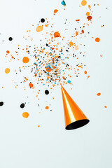 Orange party hat exploding with colorful confetti on white background for new year's eve