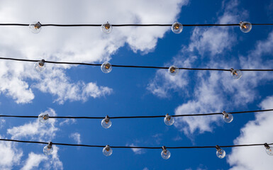 light bulbs in the street in daylight. A garland electrical wires with lamp against blue sky. Old...