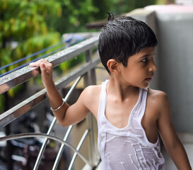 Little kid playing in summer rain in house balcony, Indian smart boy playing with rain drops during...