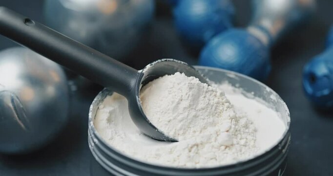 White powder in a container with a scoop, surrounded by exercise equipment
