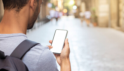 Over shoulder view of the hand holding a blank screen smartphone in a blurry city street scene.