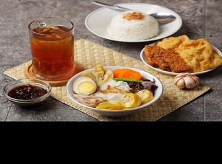 Sop ayam kampung. A bowl of free-range chicken soup with macroni, shredded chicken, sliced ​​carrots, sliced ​​wood ear mushrooms and boiled quail eggs accompanied by rice, fried food, soy sauce and a