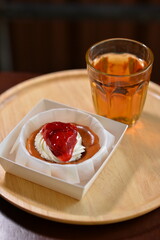 Burnt cheesecake with whipped cream and strawberry jam, served on a wooden tray with a glass of warm tea. Cozy dessert time in soft natural light.