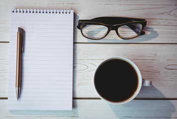Notepad by coffee cup and reading glasses