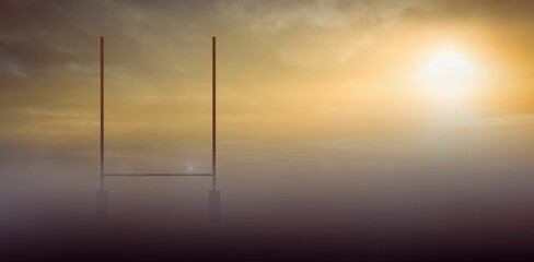 Emerging in mist, H-shaped goalposts standing on open field, sun shining through scattered clouds © vectorfusionart
