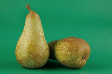 Two ripe green pears on a green background.