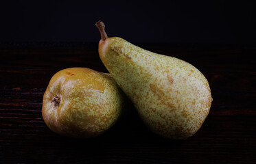 Two ripe green pears lie on a wet wooden surface covered with drops of water.